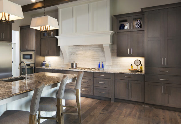 Modern kitchen with dark gray cabinets marble countertops island seating and pendant lights above the island
